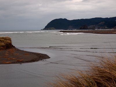 [Ripples in the water at the mouth of the river show the high tide filling the river under a completely cloud-covered sky.]